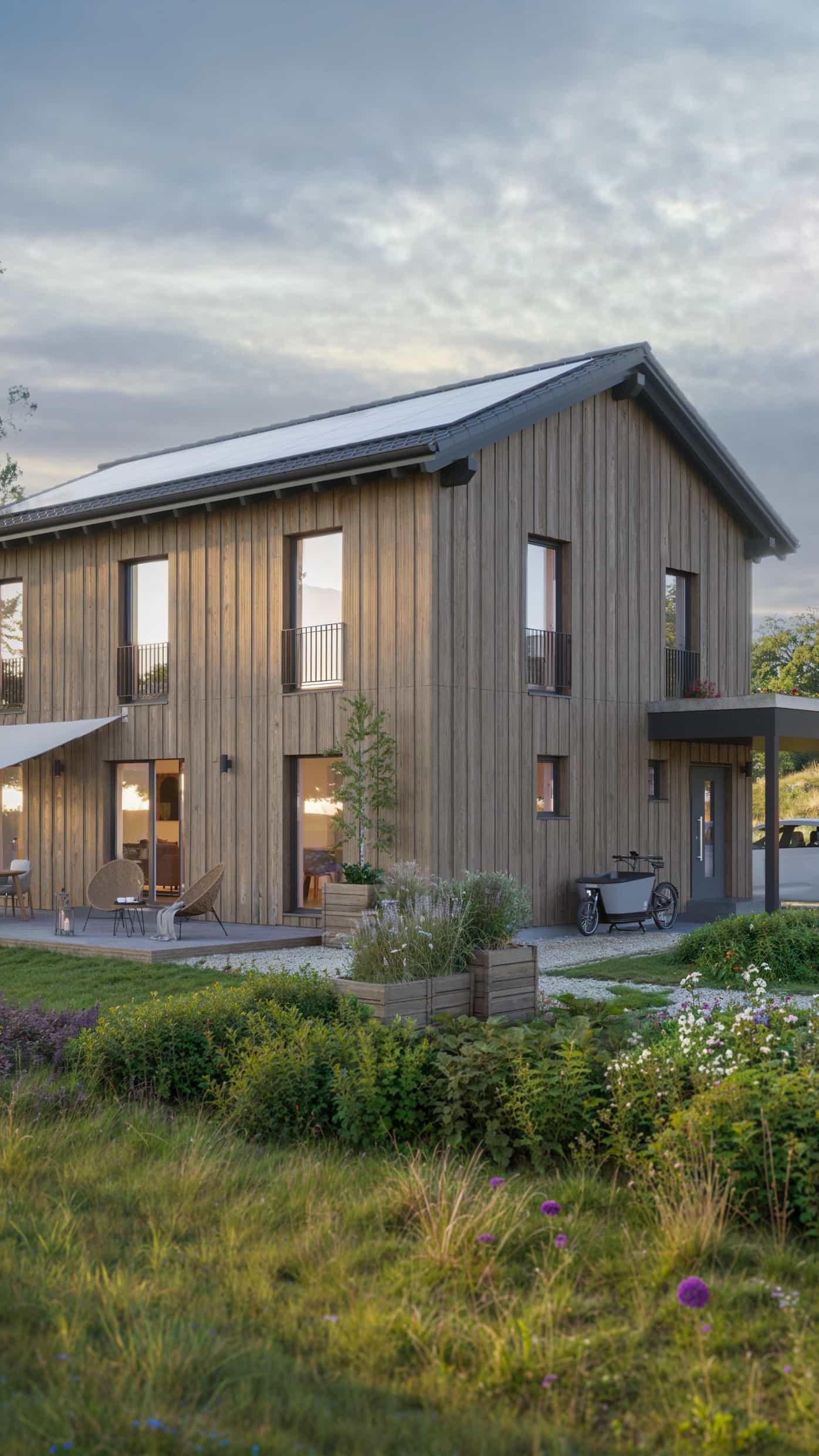 Modernes zweistöckiges Holzhaus mit Garten in ländlicher Umgebung bei Sonnenuntergang.